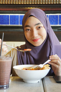 Portrait of young woman wearing hijab while eating food at restaurant