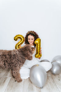 Young woman sitting with dog and balloons on floor at home