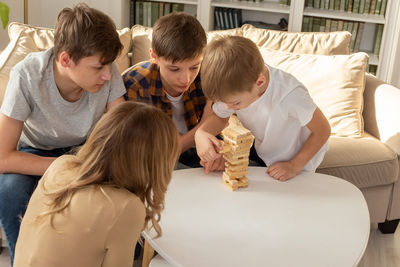 A woman and three boys are enthusiastically playing a board game made of wooden rectangular blocks