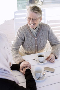 Young female home caregiver consoling senior woman while having coffee on porch