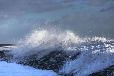 Water splashing in sea against cloudy sky