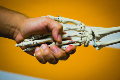 Close-up of hand holding skeleton against yellow background