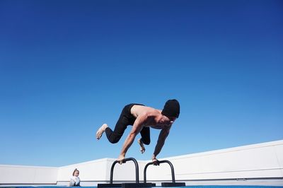 Low angle view of man jumping against clear blue sky