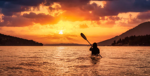 Silhouette man on sea against orange sky