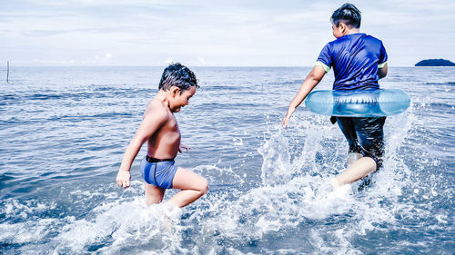 Siblings playing in sea against sky