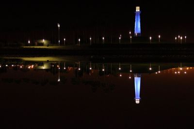 Illuminated buildings by lake against sky at night