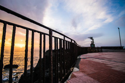 Low angle view of railing by sea against sky during sunset