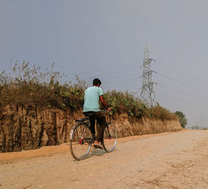 Rear view of man riding bicycle on dirt road