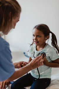 Smiling healthcare worker assisting girl in listening her own heartbeats at hospital