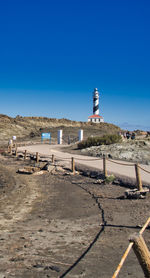 Lighthouse amidst buildings against clear blue sky