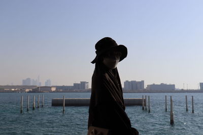 Rear view of woman standing by sea against clear sky