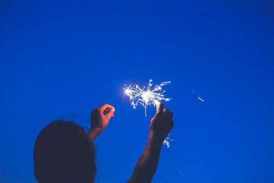 Low angle view of woman holding hands against clear blue sky