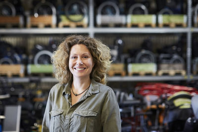 Portrait of smiling mature female worker standing against rack at warehouse