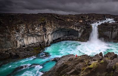 Scenic view of waterfall against stormy clouds