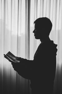 Silhouette man looking at book at home