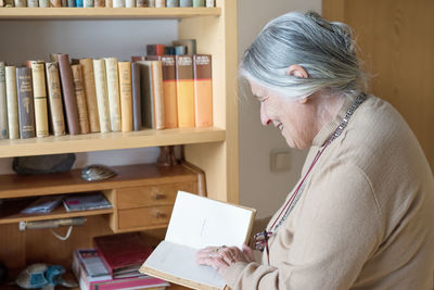 Happy senior woman reading book in library