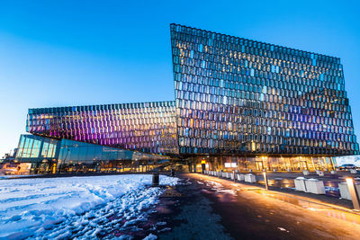 Road by illuminated buildings against clear blue sky in city