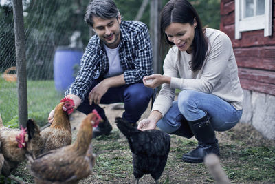 Happy couple feeding hens at poultry farm