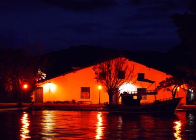 Illuminated building by lake against sky at night