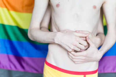 Midsection of gay couple embracing while standing against rainbow flag