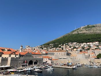 Sailboats moored by buildings in city against clear blue sky