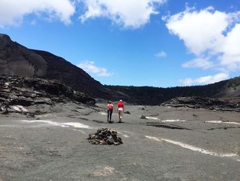 Rear view of hikers walking at kilauea iki crater against sky