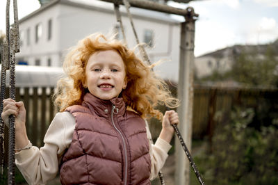 Smiling redhead girl swinging in garden