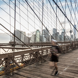 Man walking on bridge against sky in city