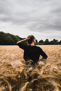 Rear view of a young woman with dark hair standing in the middle of a wheat field