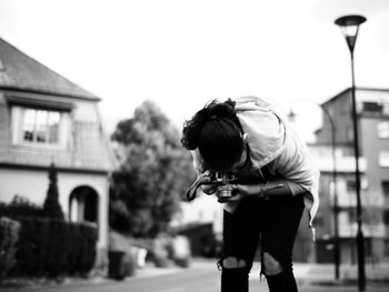 Woman photographing while standing on road in city