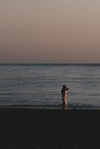 Rear view of woman standing at beach during sunset