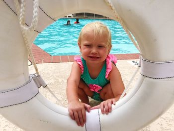 Girl holding life belt while crouching at poolside