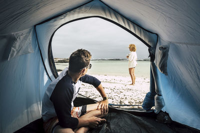 Boy sitting in tent with mother at beach