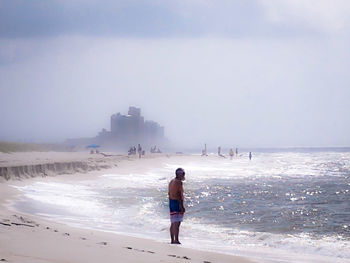 Rear view of woman standing on beach against sky