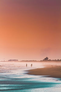 People at beach against sky during sunset