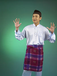 Portrait of young man in traditional clothing standing against green background