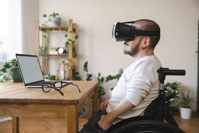 Man with disability wearing virtual reality simulator in front of laptop at home