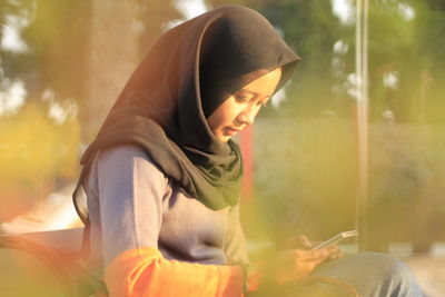 Side view of woman using mobile phone while sitting outdoors