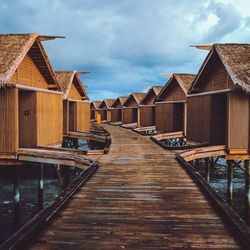 Stilt houses in row over river against cloudy sky