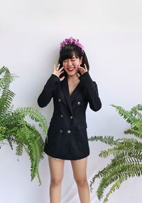 Portrait of smiling young woman wearing black suits standing against plants over white background 