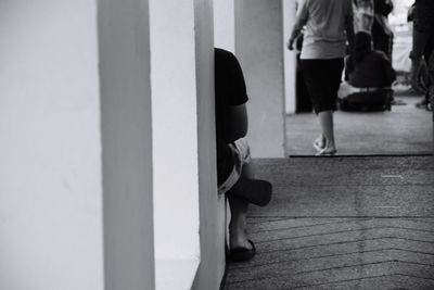 Cropped image of person sitting by wall in corridor