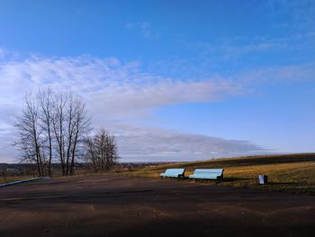Road by bare trees on field against blue sky