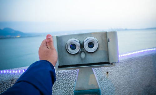 Close-up of man holding coin-operated binoculars at sea