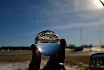 Cropped hand holding crystal ball against sky