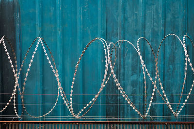 Close-up of metal barbed wire fence against blue wall