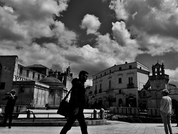 Man standing on city street against cloudy sky