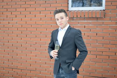 Businessman holding champagne flute and standing against brick wall