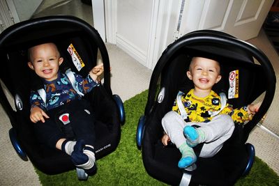 Portrait of smiling siblings, twin boys in car seats 