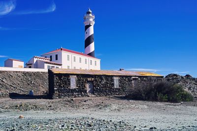 Low angle view of lighthouse against buildings against clear blue sky