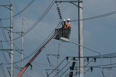 Low angle view of man working on electricity pylon against sky